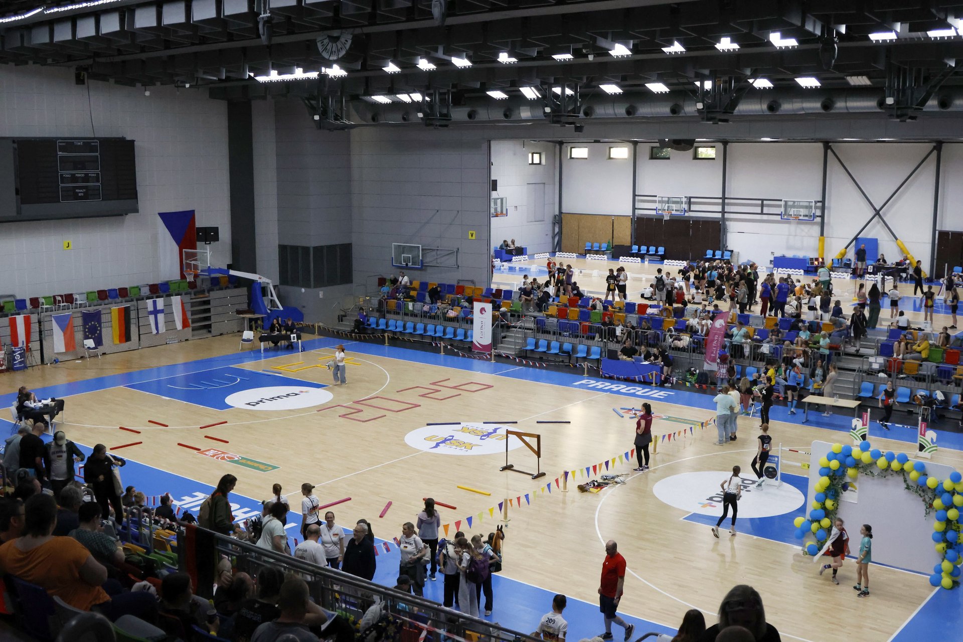 Pohled z tribuny do sportovní haly Královka v Praze během prvního ročníku European Hobby Horse Championship 2026, s vlajkami evropských zemí a hrací plochou připravenou na závody.
